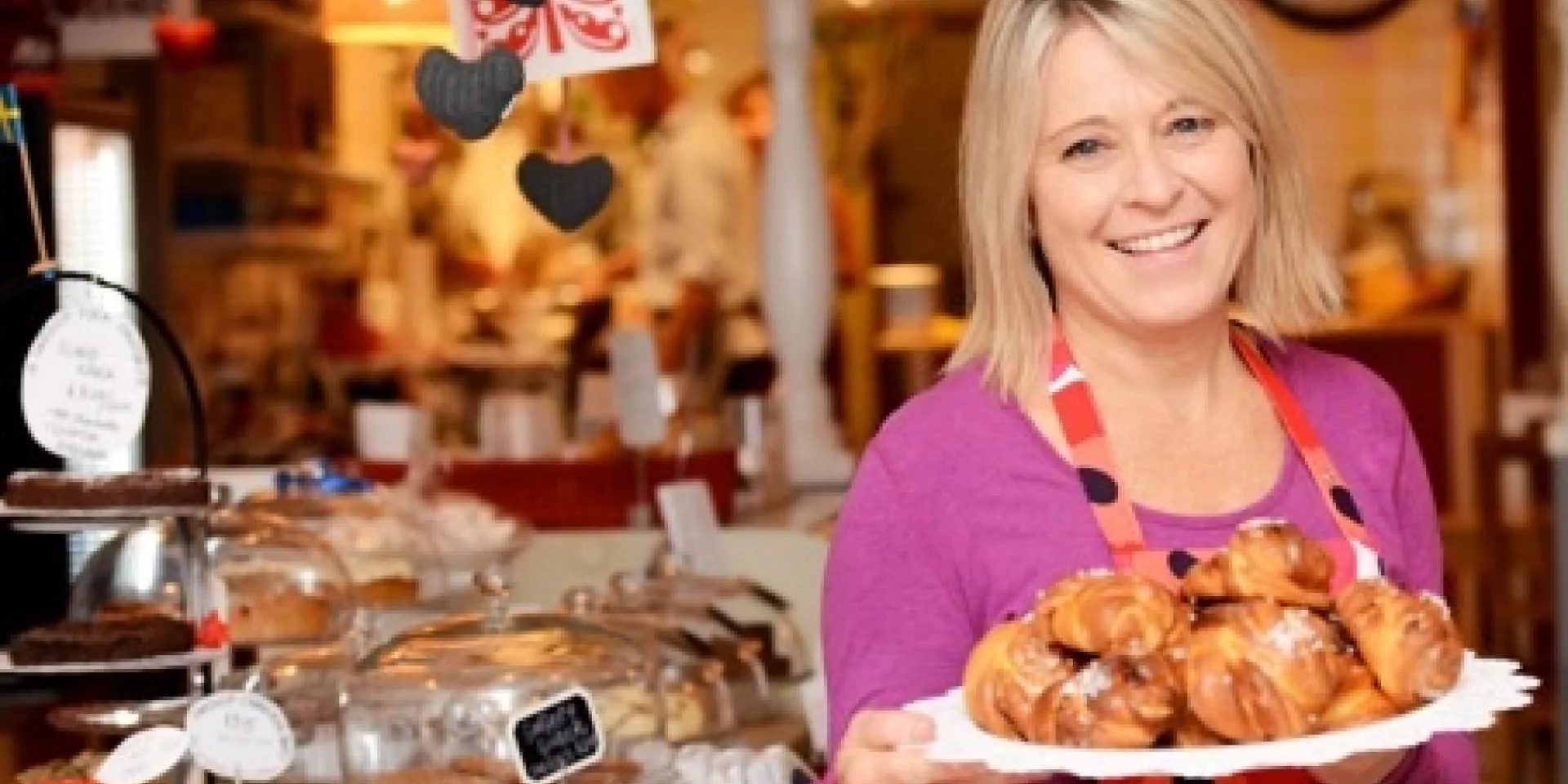 Anna Tvinnereim of Beaches Bake Shop and Cafe  young blonde woman holding a plate of pastries with bakeshop in the background