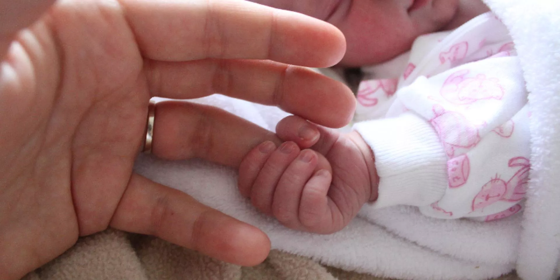 Special care nursery baby holds adult finger