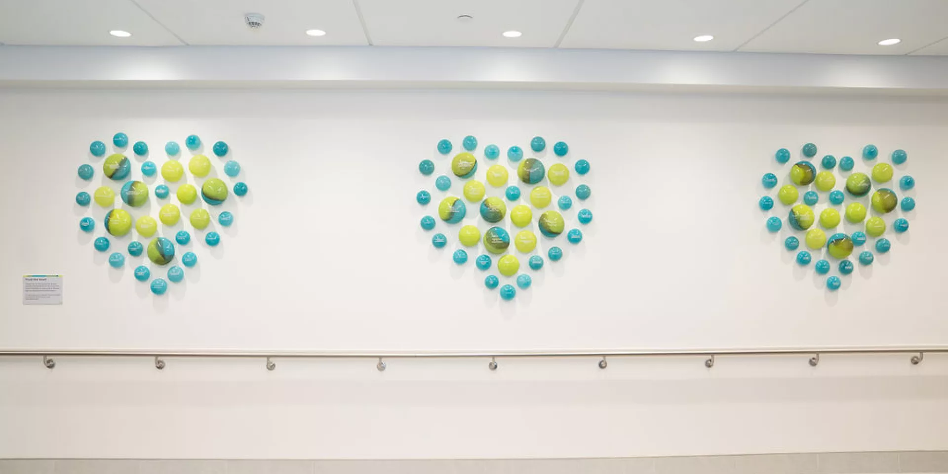 From the Heart donors are celebrated with engraved glass orbs, displayed in our Ken and Marilyn Thomson Patient Care Centre lobby. a wall with blue and green glass orbs making up three hearts on the wall, engraved with donor names.