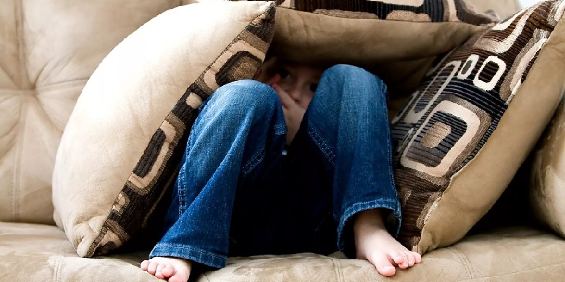 little boy on couch  little boy sitting on couch with knees up looking ahead mostly covered up with throw cushions