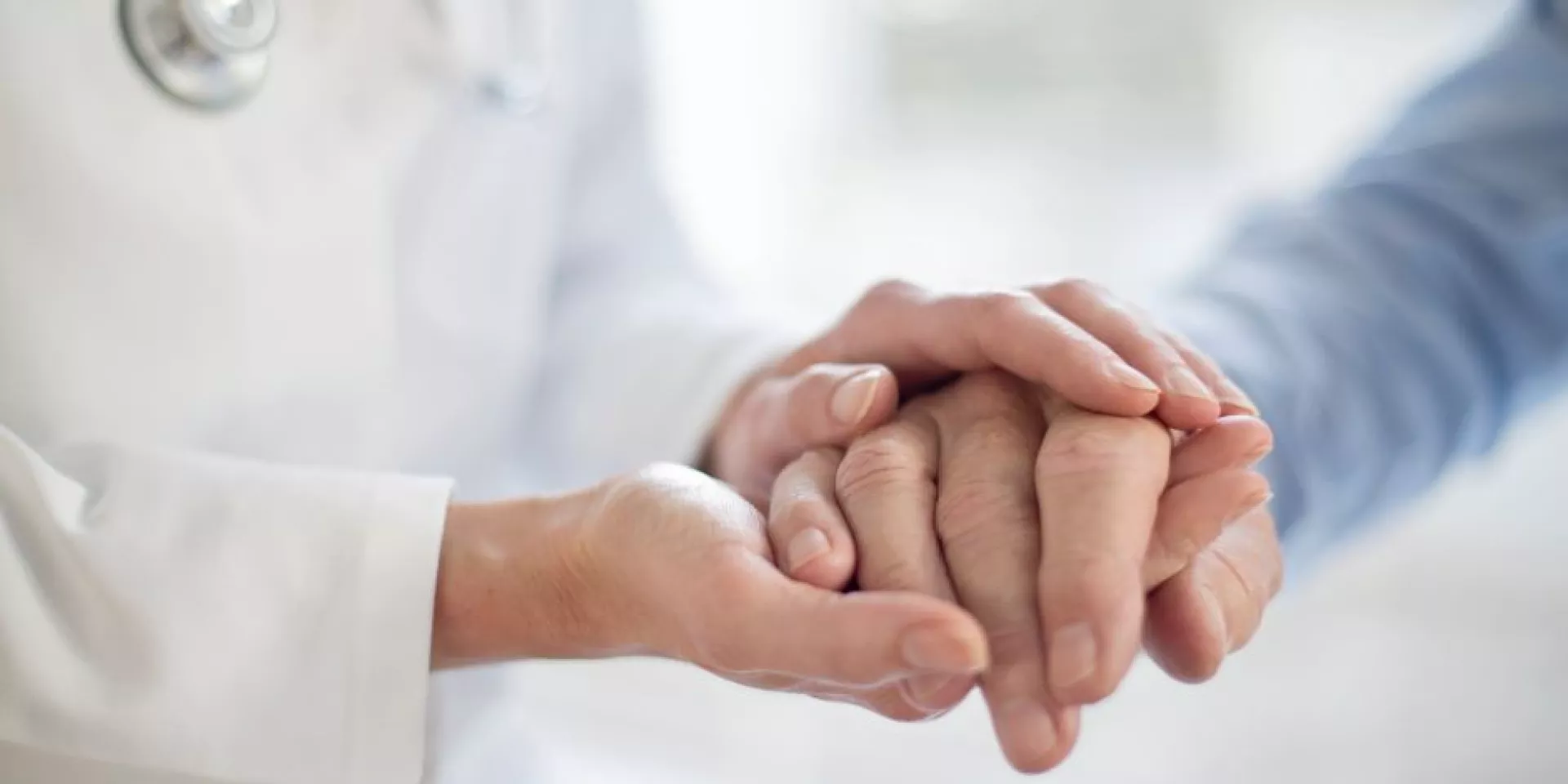A close up of a physician and patient holding hands