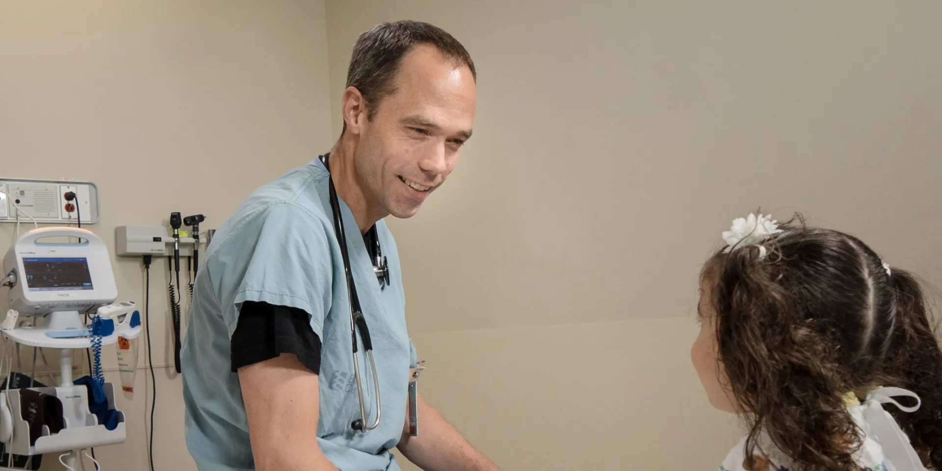 Dr. Paul Hannam sitting on a hospital bed, speaking with a young patient