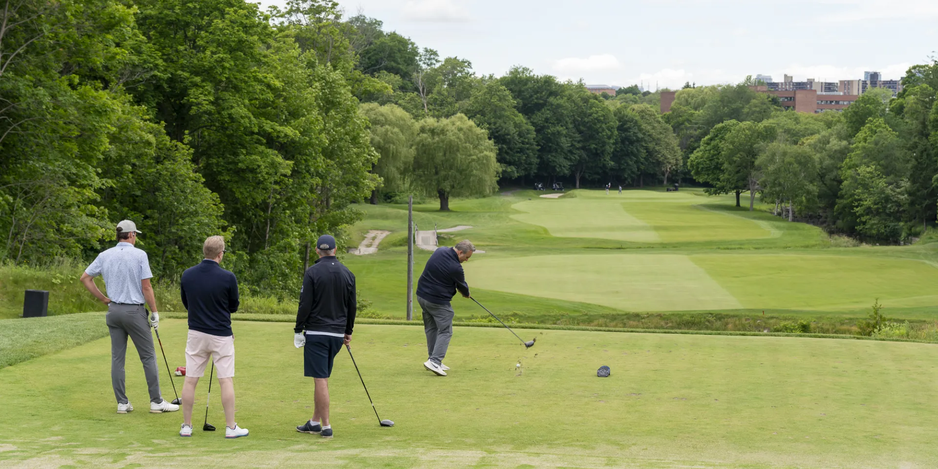 Four men on a golf course, with lush trees around the green