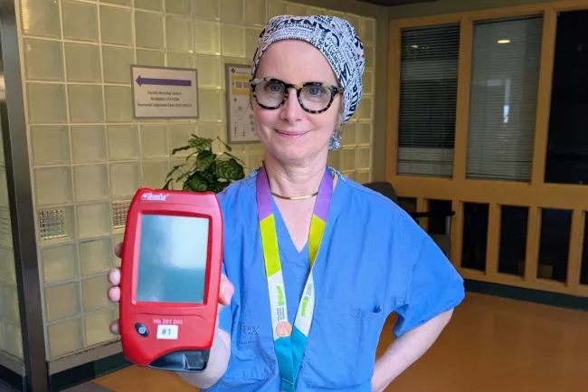 Dr. Elin Raymond, Chief of Obstetrics and Gynaecology and Medical Co-Director of Maternal, Newborn and Child Services, holds a red, palm-sized, HemoCue machine. It allows fast and accurate assessment of blood loss.