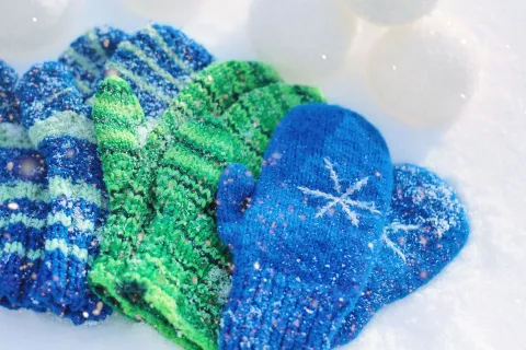 Three pairs of blue and green mittens in the snow